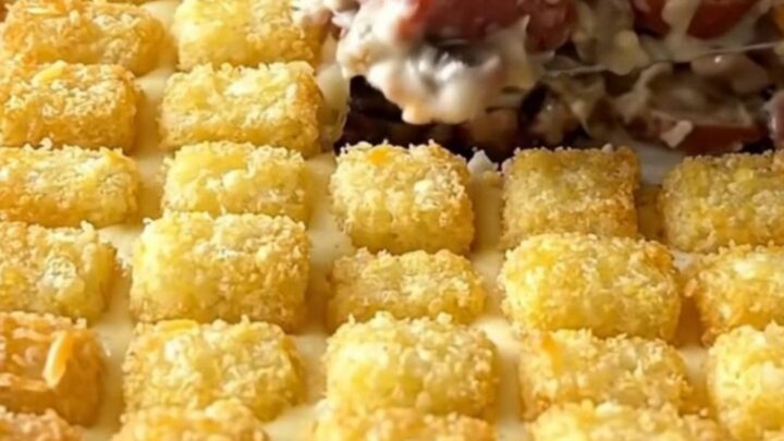 A ceramic baking dish filled with a creamy mushroom sausage hotdish topped with golden brown potato tots.