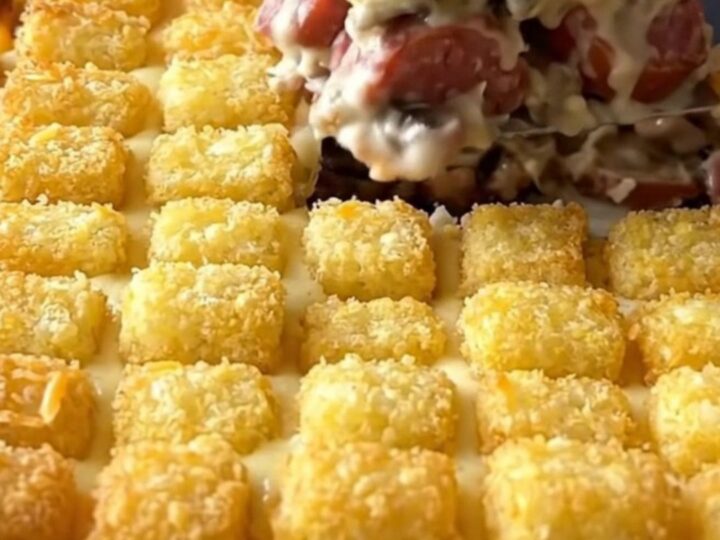 A ceramic baking dish filled with a creamy mushroom sausage hotdish topped with golden brown potato tots.