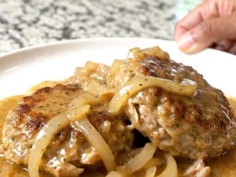 A close-up of tender ground turkey patties covered in creamy country gravy and onion slices on a plate.