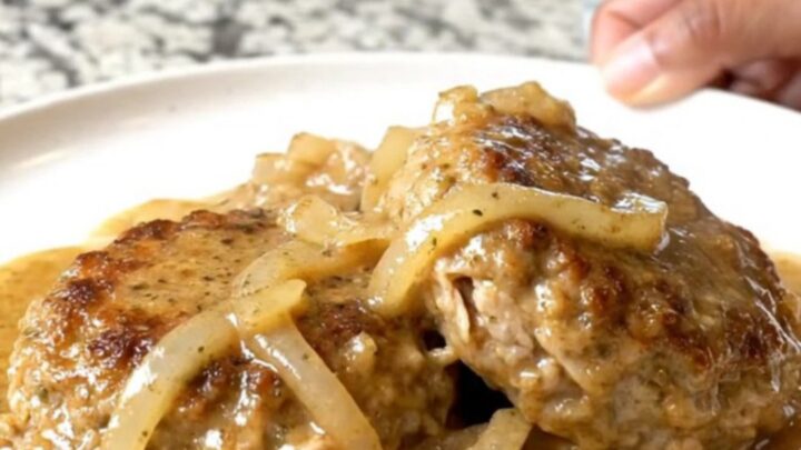 A close-up of tender ground turkey patties covered in creamy country gravy and onion slices on a plate.