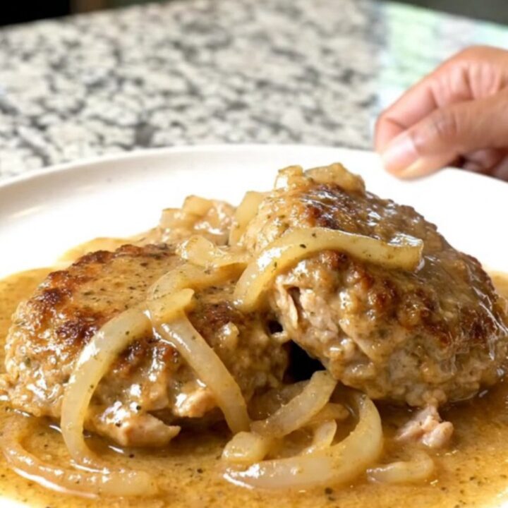 A close-up of tender ground turkey patties covered in creamy country gravy and onion slices on a plate.