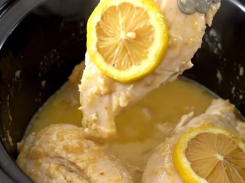 Tender chicken breasts in a slow cooker topped with lemon slices and herbs.