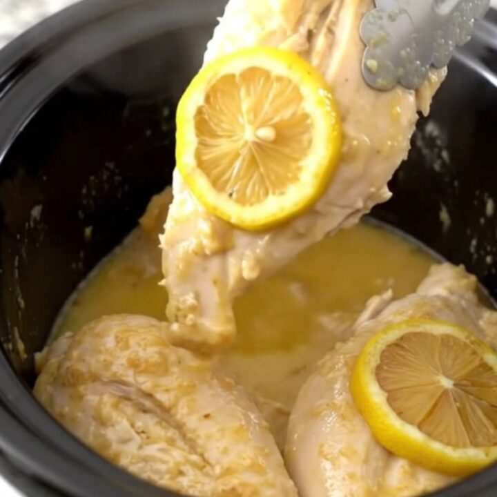 Tender chicken breasts in a slow cooker topped with lemon slices and herbs.