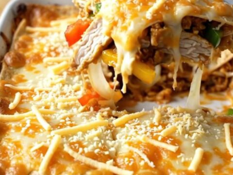 A large rectangular baking dish filled with a golden, bubbly chicken fajita tortilla bake on a wooden table.