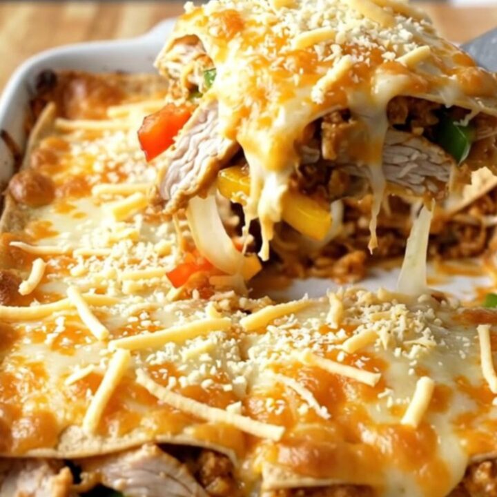 A large rectangular baking dish filled with a golden, bubbly chicken fajita tortilla bake on a wooden table.
