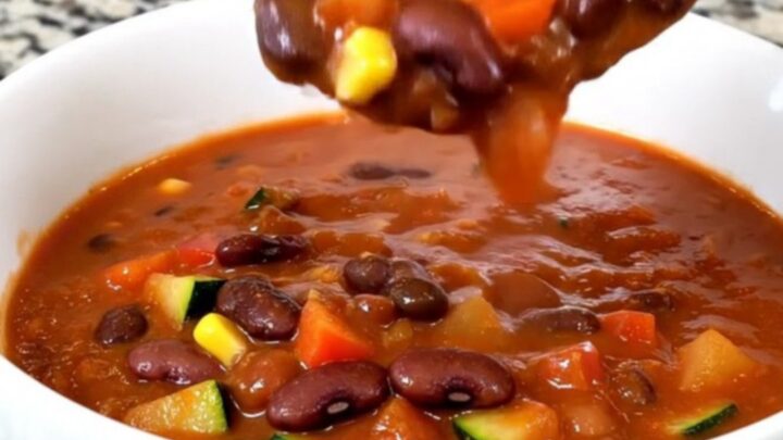 A top-down view of a black slow cooker filled with a vibrant, colorful mixture of beans, diced zucchini, peppers, and corn.