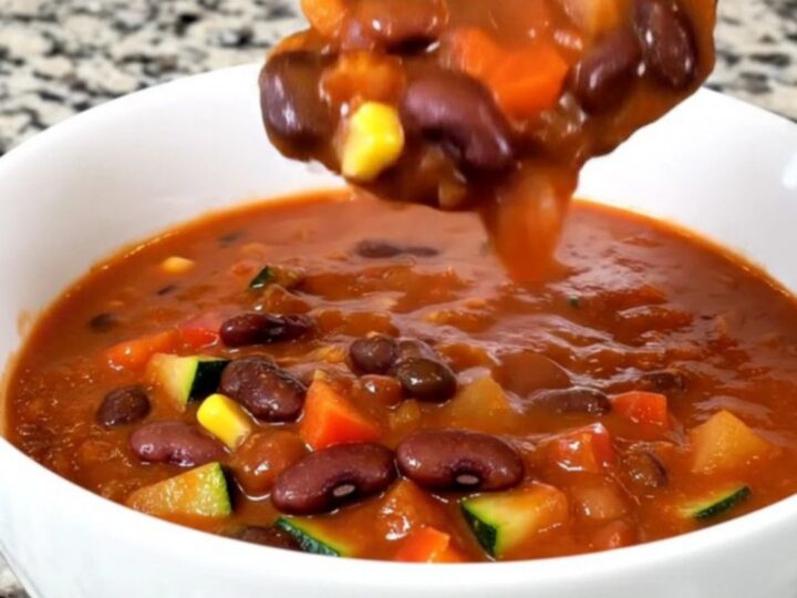 A top-down view of a black slow cooker filled with a vibrant, colorful mixture of beans, diced zucchini, peppers, and corn.