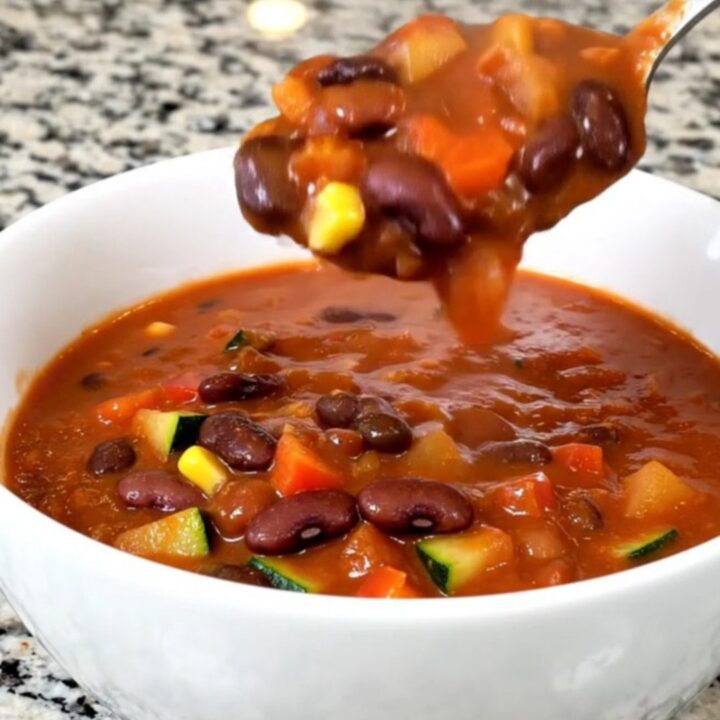 A top-down view of a black slow cooker filled with a vibrant, colorful mixture of beans, diced zucchini, peppers, and corn.