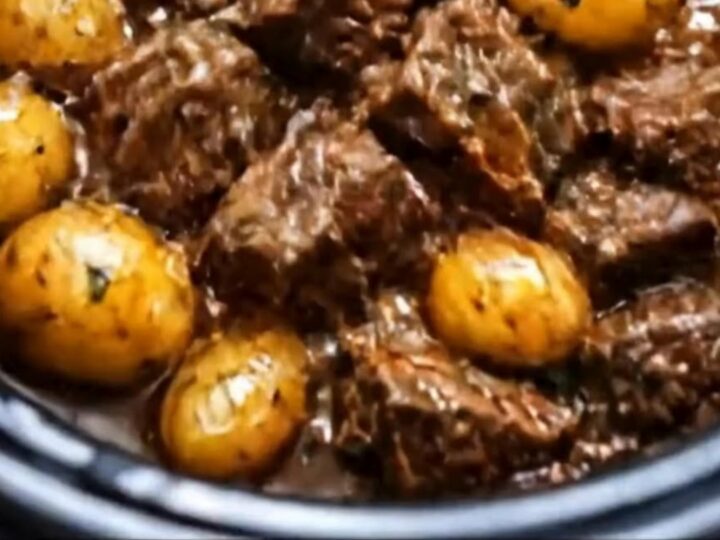 A slow cooker filled with tender, glossy garlic butter beef bites and round baby potatoes in a rich gravy.