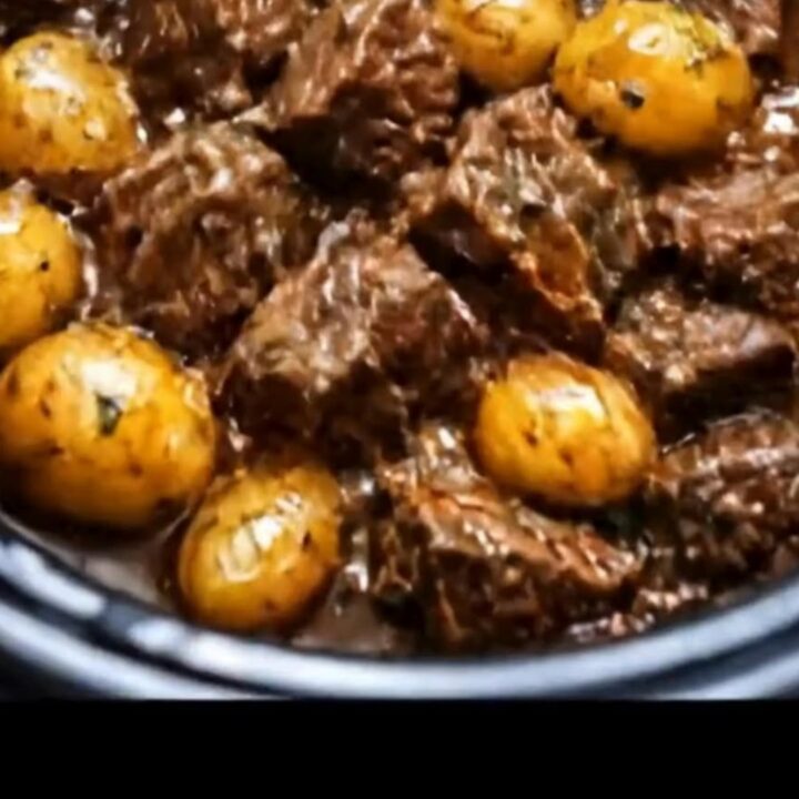 A slow cooker filled with tender, glossy garlic butter beef bites and round baby potatoes in a rich gravy.