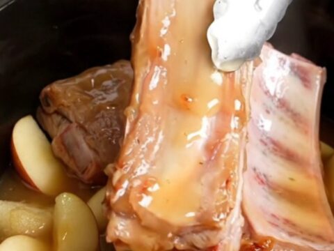 A close-up view into a slow cooker filled with tender, golden-tan country-style pork ribs, soft apple wedges, and a thick