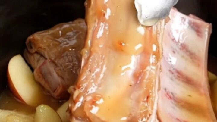 A close-up view into a slow cooker filled with tender, golden-tan country-style pork ribs, soft apple wedges, and a thick