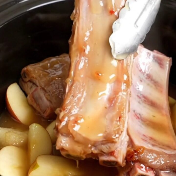 A close-up view into a slow cooker filled with tender, golden-tan country-style pork ribs, soft apple wedges, and a thick