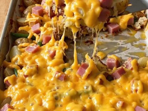 A golden sheet pan filled with roasted ham cubes, baby potatoes, and green beans topped with melted cheddar cheese.
