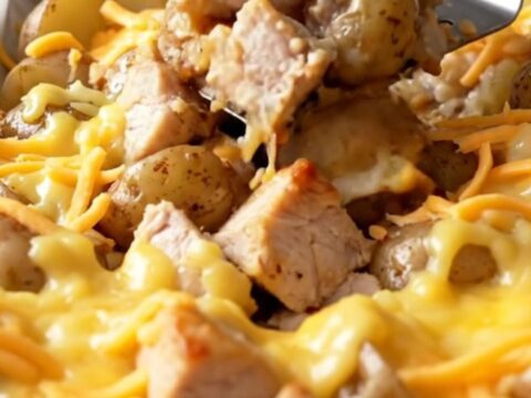 A sheet pan filled with roasted chicken chunks and baby potatoes topped with melted cheddar cheese.