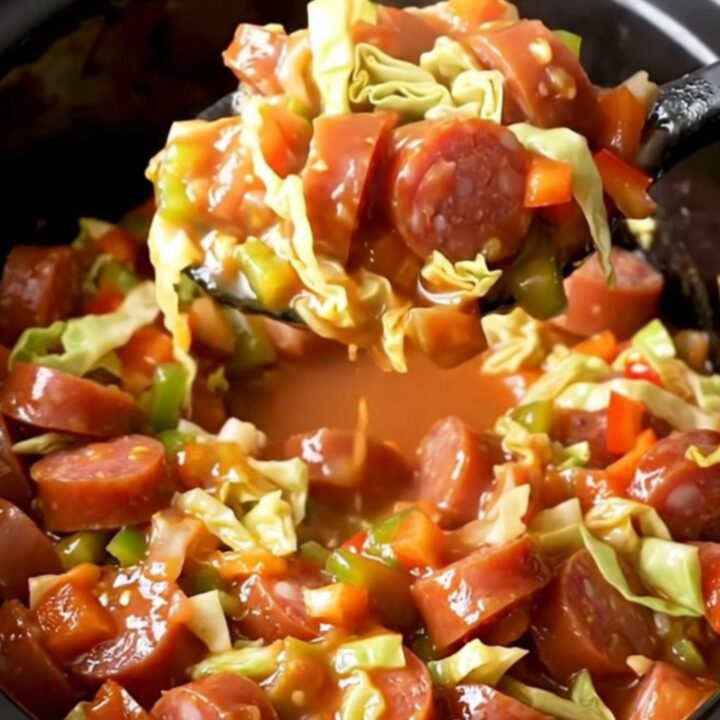 A close-up of the slow cooker filled with tender green cabbage, red and green bell peppers