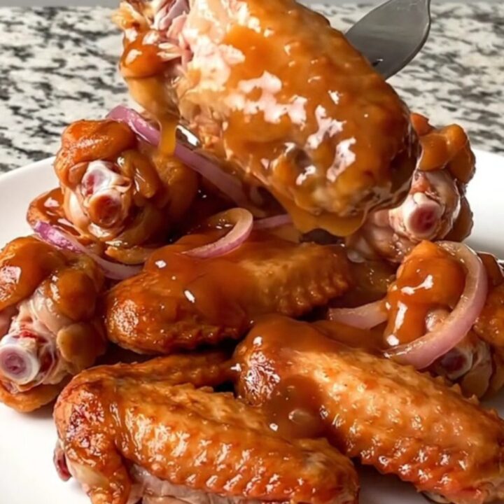 A platter of slow-cooked chicken wings coated in a glossy, dark reddish-brown maple chipotle glaze.