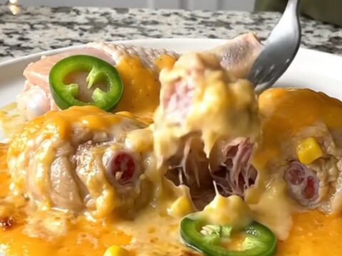 A close-up of tender chicken drumsticks smothered in a creamy corn and cheese sauce with jalapeno slices.