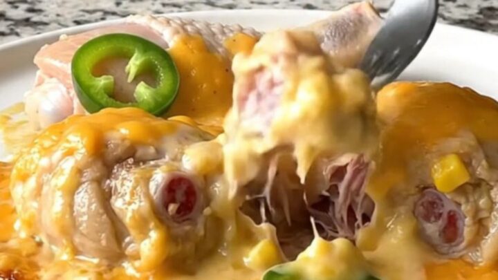 A close-up of tender chicken drumsticks smothered in a creamy corn and cheese sauce with jalapeno slices.