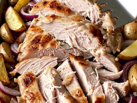 A sheet pan filled with golden roasted potato wedges, tender red onions, and a sliced turkey slab, topped with crumbled feta.