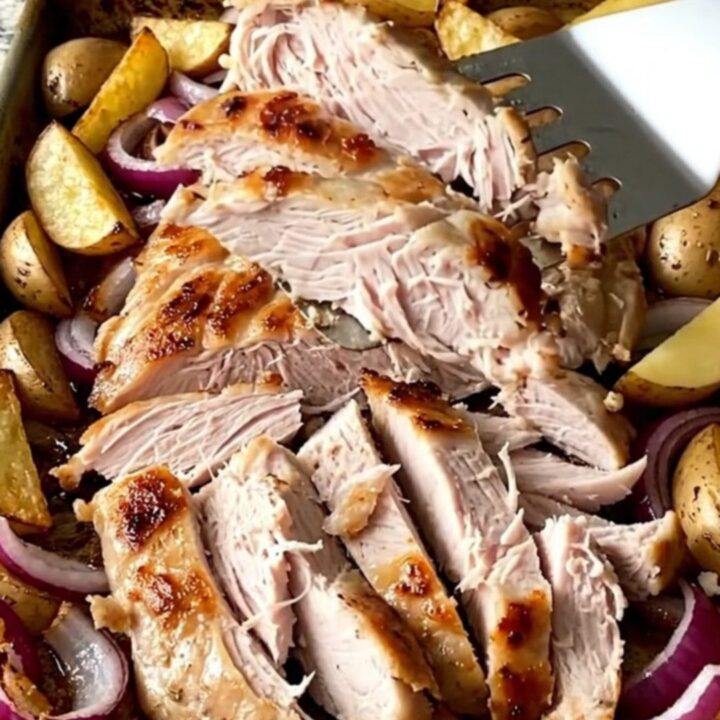 A sheet pan filled with golden roasted potato wedges, tender red onions, and a sliced turkey slab, topped with crumbled feta.