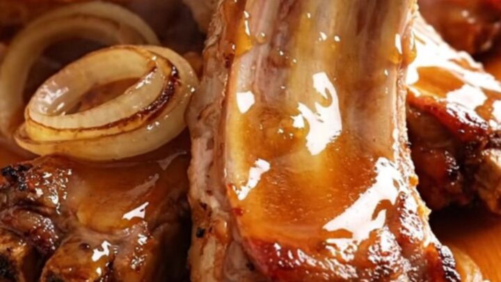 A close-up of tender, glazed pork spareribs arranged on a wooden board with a shiny, thick honey sauce.