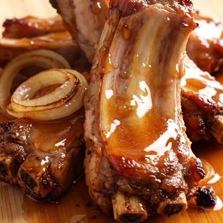 A close-up of tender, glazed pork spareribs arranged on a wooden board with a shiny, thick honey sauce.