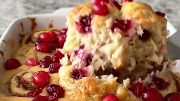 A golden, baked cranberry orange cinnamon roll dish in a white ceramic pan on a granite counter.