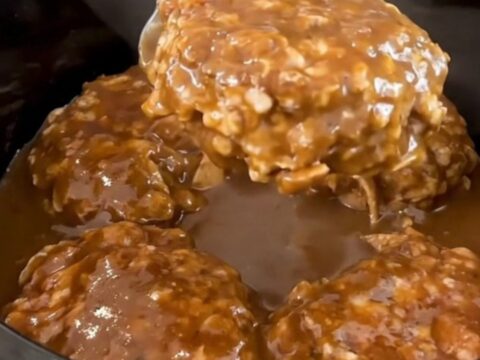 A close-up of slow-cooked turkey burger steaks smothered in a rich, dark peppercorn gravy inside a slow cooker.
