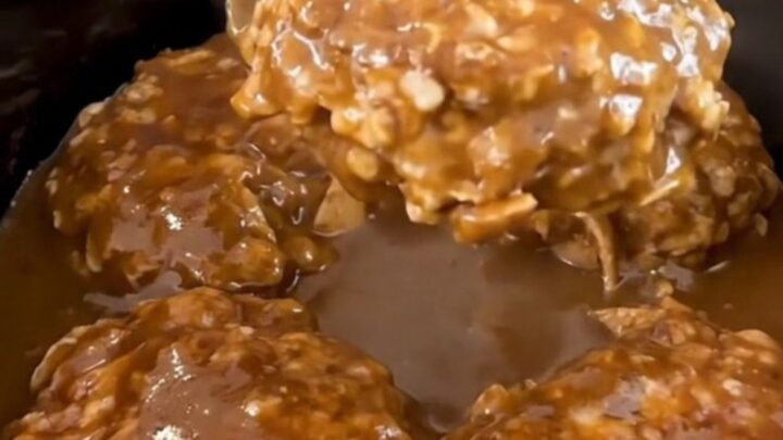 A close-up of slow-cooked turkey burger steaks smothered in a rich, dark peppercorn gravy inside a slow cooker.