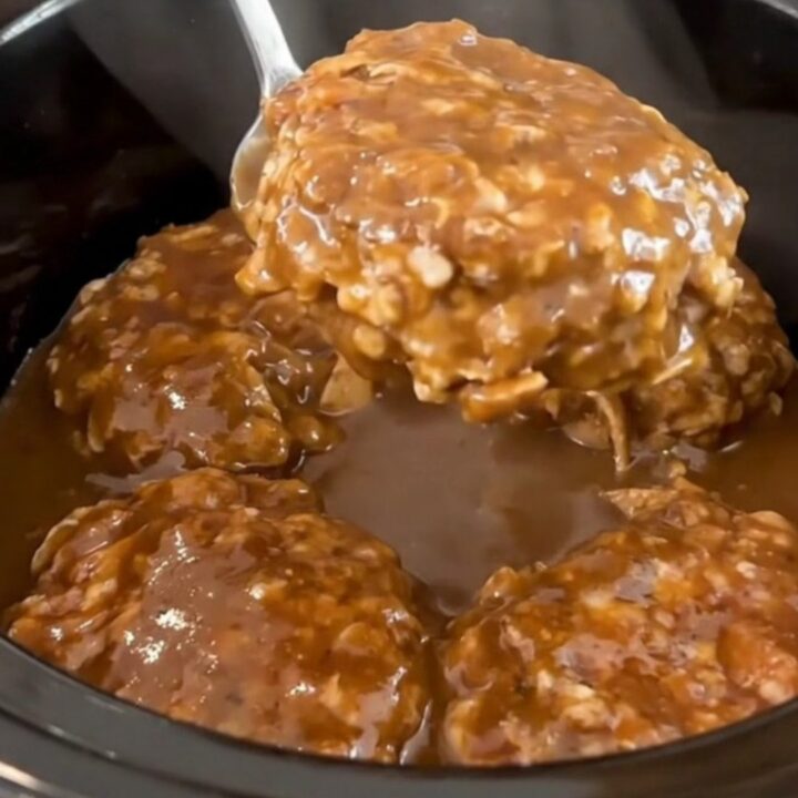 A close-up of slow-cooked turkey burger steaks smothered in a rich, dark peppercorn gravy inside a slow cooker.