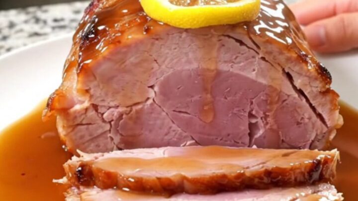 A beautifully glazed slow cooker ham topped with lemon slices, served on a white platter.
