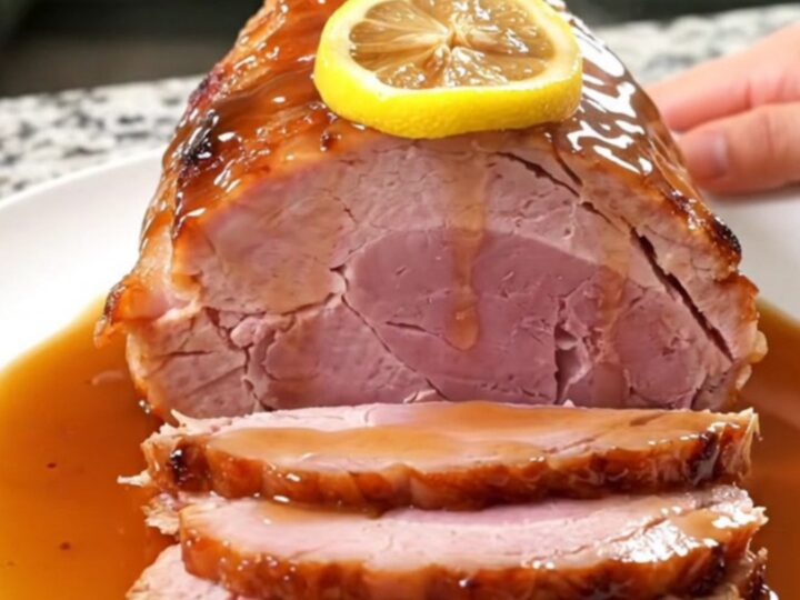 A beautifully glazed slow cooker ham topped with lemon slices, served on a white platter.