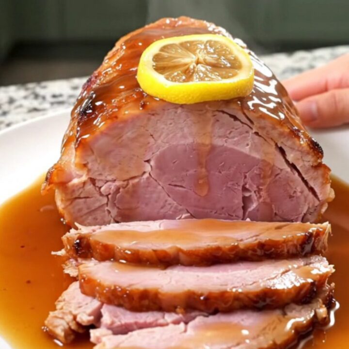 A beautifully glazed slow cooker ham topped with lemon slices, served on a white platter.