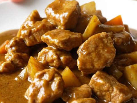 A bowl of Japanese pork curry with chunks of pork, carrots, and potatoes in a thick brown sauce over white rice.