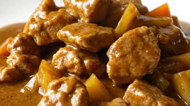 A bowl of Japanese pork curry with chunks of pork, carrots, and potatoes in a thick brown sauce over white rice.