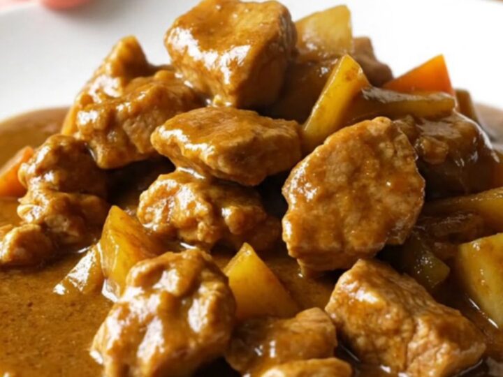 A bowl of Japanese pork curry with chunks of pork, carrots, and potatoes in a thick brown sauce over white rice.