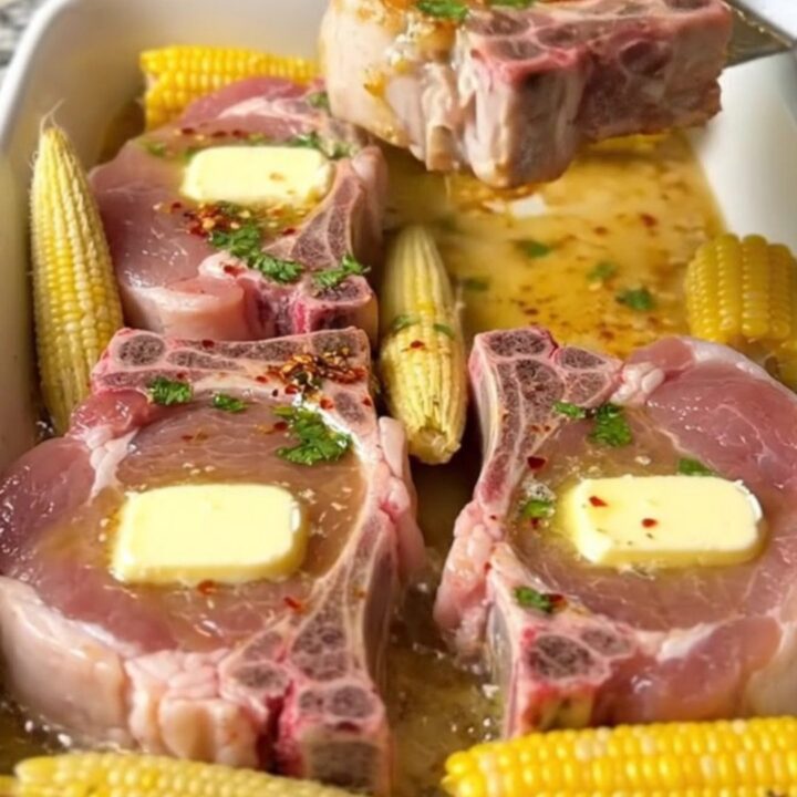 A large ceramic baking dish filled with golden-brown bone-in pork chops and mini corn cobs in a cilantro lime butter sauce.