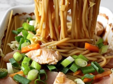 A large white rectangular baking dish filled with cooked spaghetti, chicken strips, carrots, and cabbage