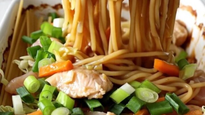 A large white rectangular baking dish filled with cooked spaghetti, chicken strips, carrots, and cabbage