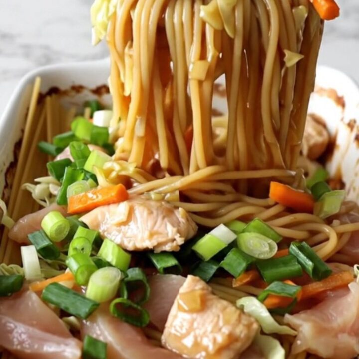 A large white rectangular baking dish filled with cooked spaghetti, chicken strips, carrots, and cabbage