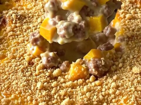 A top-down view of a creamy sausage and yellow squash casserole in a white baking dish, topped with golden crumbs.