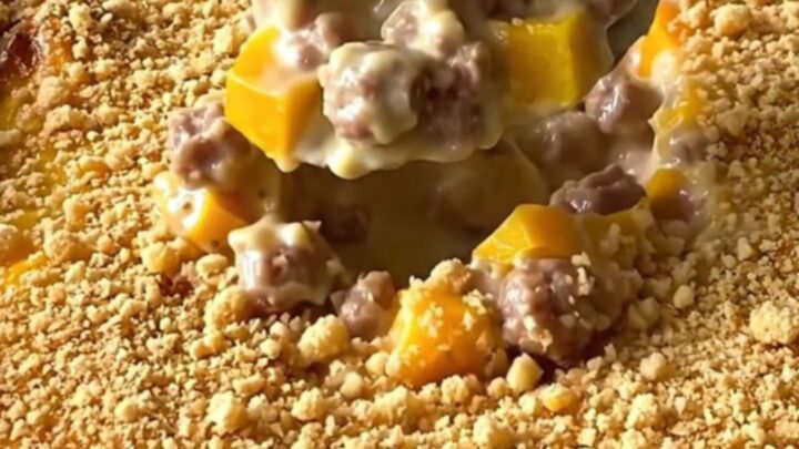 A top-down view of a creamy sausage and yellow squash casserole in a white baking dish, topped with golden crumbs.