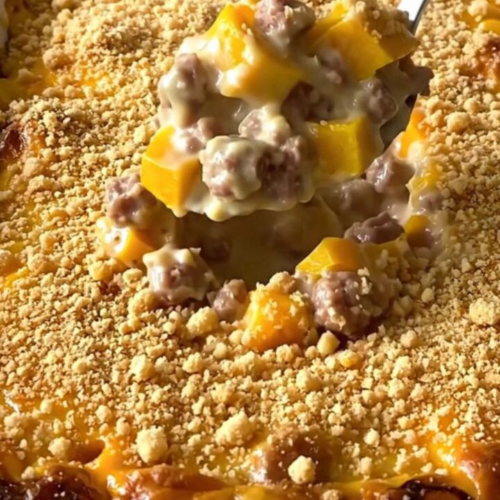 A top-down view of a creamy sausage and yellow squash casserole in a white baking dish, topped with golden crumbs.