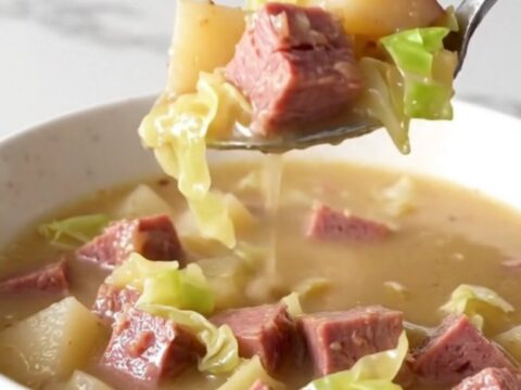 A steaming bowl of creamy corned beef and cabbage chowder served in a plain white bowl on a quartz countertop.