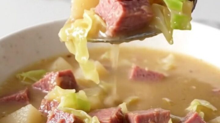 A steaming bowl of creamy corned beef and cabbage chowder served in a plain white bowl on a quartz countertop.
