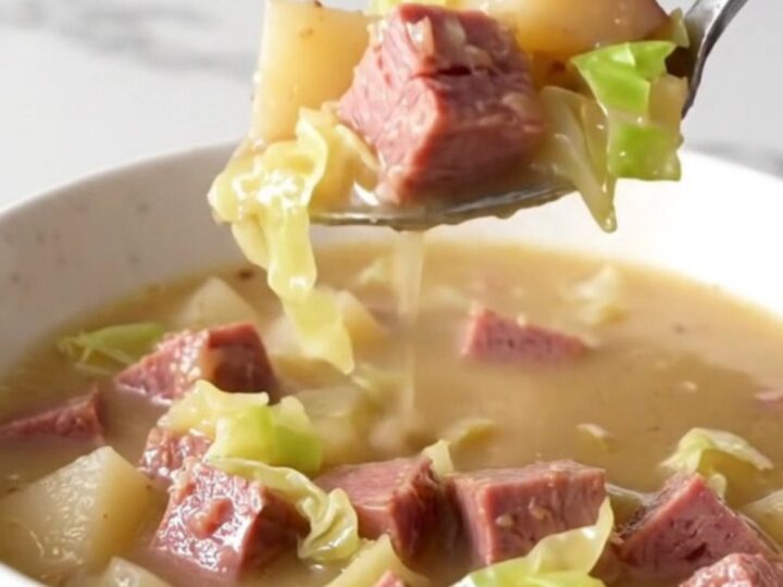 A steaming bowl of creamy corned beef and cabbage chowder served in a plain white bowl on a quartz countertop.