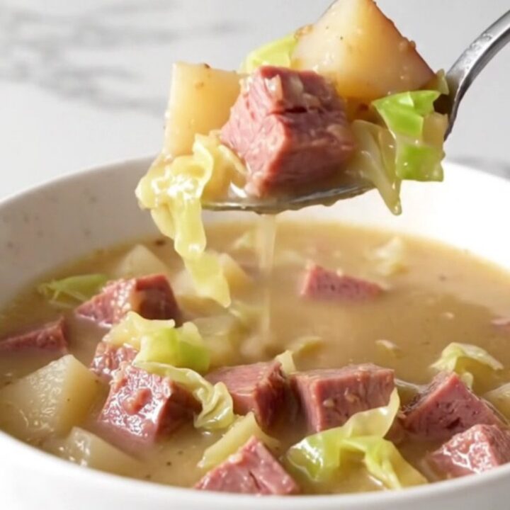 A steaming bowl of creamy corned beef and cabbage chowder served in a plain white bowl on a quartz countertop.