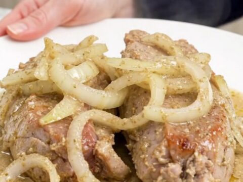A close-up view of cooked pork tenderloin slices topped with a thick, creamy horseradish sauce on a white plate.