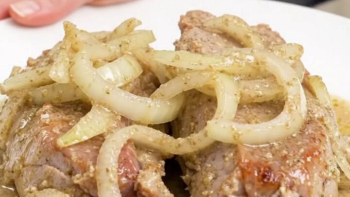 A close-up view of cooked pork tenderloin slices topped with a thick, creamy horseradish sauce on a white plate.